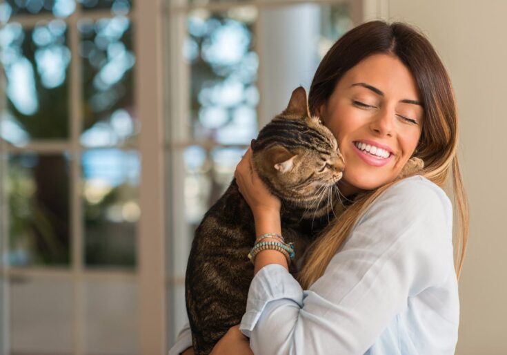 Young beautiful woman smiling and cuddling cat with love at home
