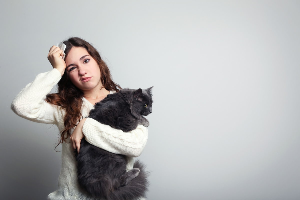 Young woman with allergy holding cat on grey background