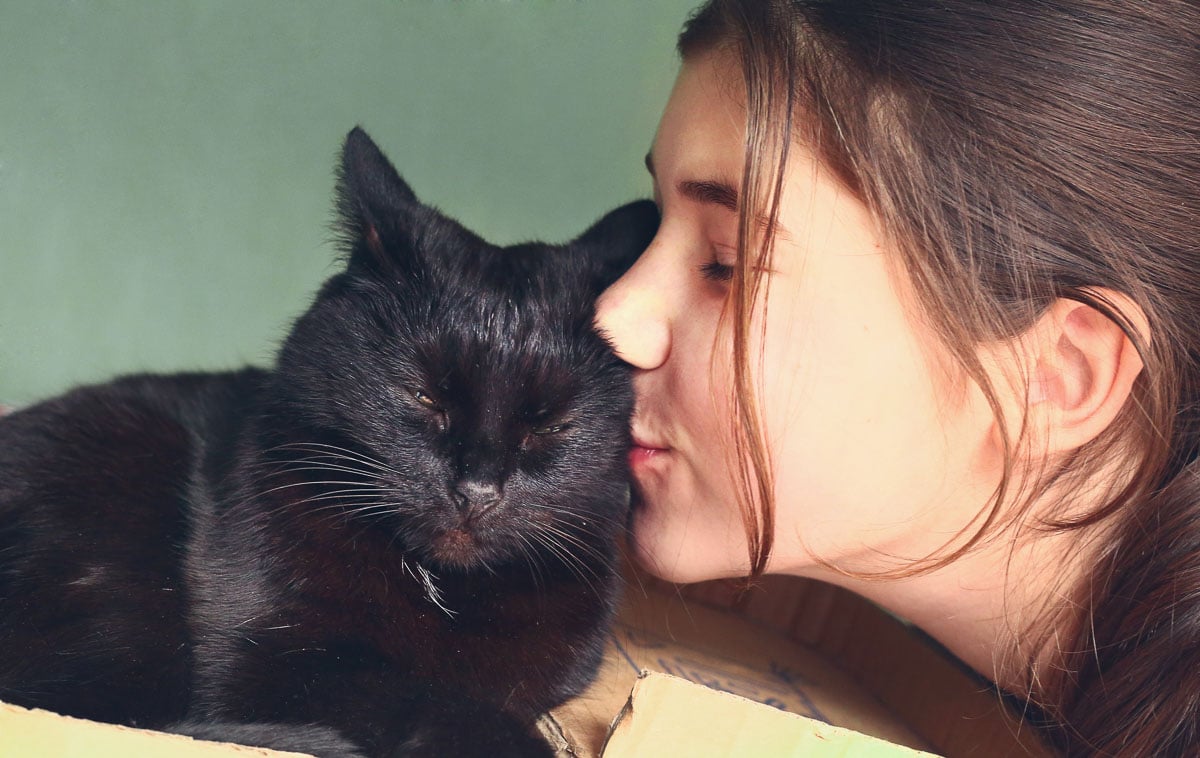 A close up image of a teenage girl kissing a black cat.