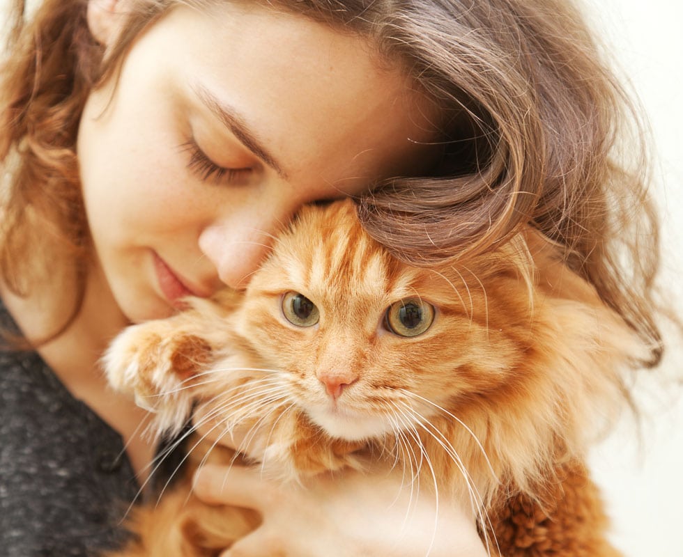 Woman cuddling a ginger cat.