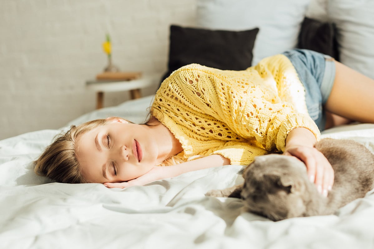 Why Do Cats Sleep Next to Their Owners? (2022) 7 Reasons For Cuddles 5 Woman asleep on bed with one arm reached out to sleeping cat.
