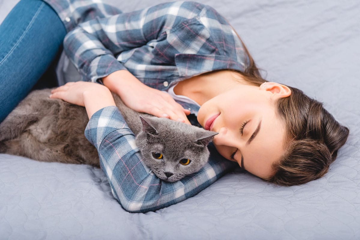 woman asleep with grey cat in her arms from a distance