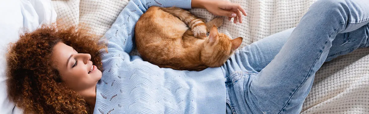 woman lying on bed with ginger cat curled up under her arm