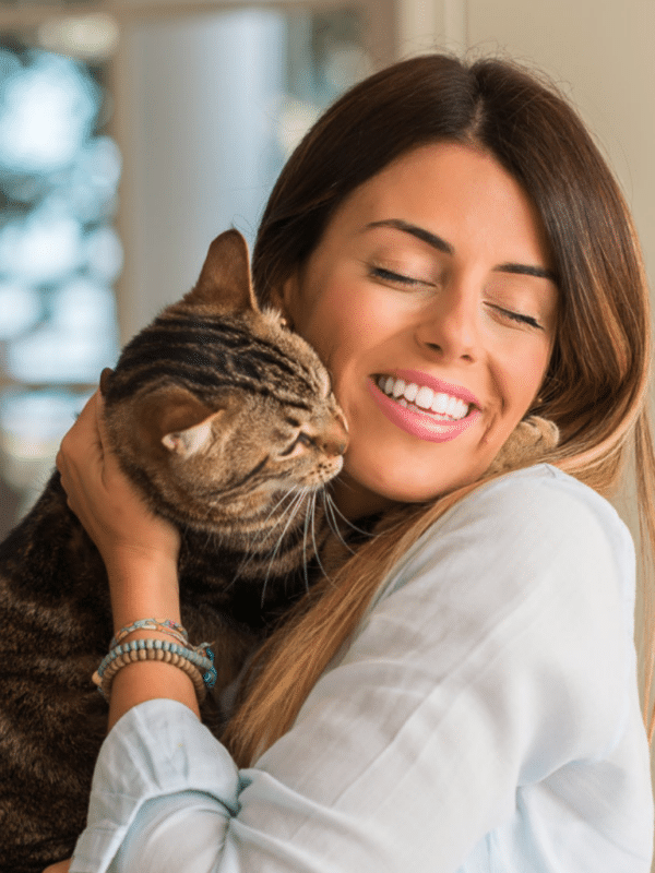 woman with brown hair cuddling tabby cat